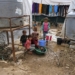 Children sit by as a woman washes dishes in a plastic basin outside a tent at a make-shift camp for Syrian refugees in Talhayat in the Akkar district in north Lebanon on October 26, 2022. (Photo by Ibrahim Chalhoub / AFP)