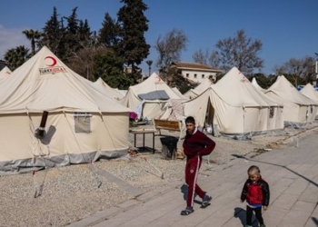 Children walk past tents in a makeshift camp in Antakya, southern Turkey, on February 22, 2023. - A 6.4-magnitude earthquake has rocked Turkey's southern province of Hatay and northern Syria, killing six people and sparking fresh panic after a massive February 6 tremor left nearly 45,000 dead in both countries. (Photo by Sameer Al-DOUMY / AFP)