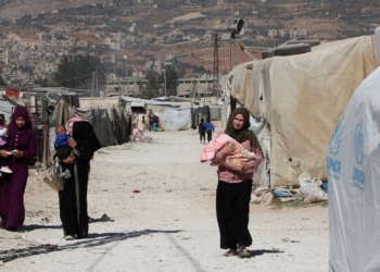 Syrian refugee women carry children as they walk at an informal camp, in the Bekaa Valley, Lebanon October 18, 2022. REUTERS/Mohamed Azakir