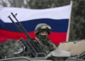 A pro-Russian man (not seen) holds a Russian flag behind an armed servicemen on top of a Russian army vehicle outside a Ukrainian border guard post in the Crimean town of Balaclava March 1, 2014. Ukraine accused Russia on Saturday of sending thousands of extra troops to Crimea and placed its military in the area on high alert as the Black Sea peninsula appeared to slip beyond Kiev's control. REUTERS/Baz Ratner (UKRAINE - Tags: MILITARY POLITICS CIVIL UNREST)