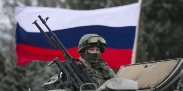 A pro-Russian man (not seen) holds a Russian flag behind an armed servicemen on top of a Russian army vehicle outside a Ukrainian border guard post in the Crimean town of Balaclava March 1, 2014. Ukraine accused Russia on Saturday of sending thousands of extra troops to Crimea and placed its military in the area on high alert as the Black Sea peninsula appeared to slip beyond Kiev's control. REUTERS/Baz Ratner (UKRAINE - Tags: MILITARY POLITICS CIVIL UNREST)