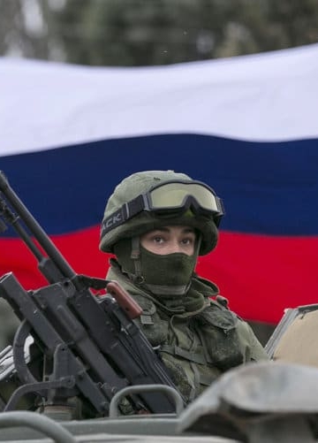 A pro-Russian man (not seen) holds a Russian flag behind an armed servicemen on top of a Russian army vehicle outside a Ukrainian border guard post in the Crimean town of Balaclava March 1, 2014. Ukraine accused Russia on Saturday of sending thousands of extra troops to Crimea and placed its military in the area on high alert as the Black Sea peninsula appeared to slip beyond Kiev's control. REUTERS/Baz Ratner (UKRAINE - Tags: MILITARY POLITICS CIVIL UNREST)