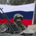 A pro-Russian man (not seen) holds a Russian flag behind an armed servicemen on top of a Russian army vehicle outside a Ukrainian border guard post in the Crimean town of Balaclava March 1, 2014. Ukraine accused Russia on Saturday of sending thousands of extra troops to Crimea and placed its military in the area on high alert as the Black Sea peninsula appeared to slip beyond Kiev's control. REUTERS/Baz Ratner (UKRAINE - Tags: MILITARY POLITICS CIVIL UNREST)